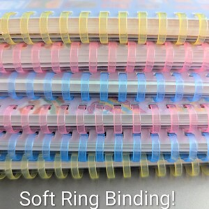 May include: Close-up of a stack of notebooks with soft ring binding. The spiral bindings are in yellow, pink, and blue. The text "Soft Ring Binding!" is at the bottom of the image.