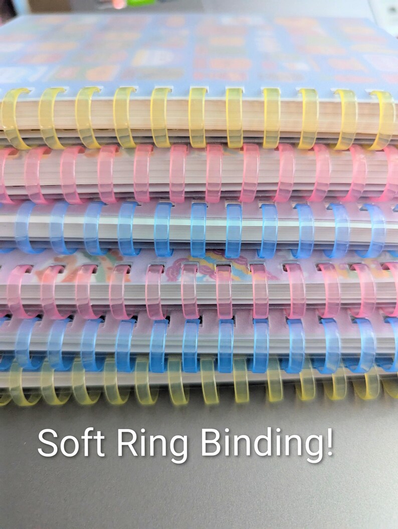 May include: Close-up of a stack of notebooks with soft ring binding. The spiral bindings are in yellow, pink, and blue. The text "Soft Ring Binding!" is at the bottom of the image.