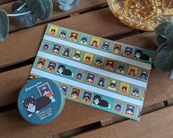 May include: A roll of washi tape and a matching sheet of paper featuring a repeating pattern of tuxedo cats in framed portraits. The tape is labelled "Framed Cats Washi Tape 15mm x 10m". The background is a wooden surface.