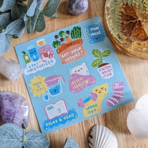 May include: A blue card with colorful illustrations and text. The text includes "Stay moisturized", "Eat your veggies", "Sleep early", "Enjoy your time", "Take a sip", "Relax & read", "Work out", and "Be cozy".