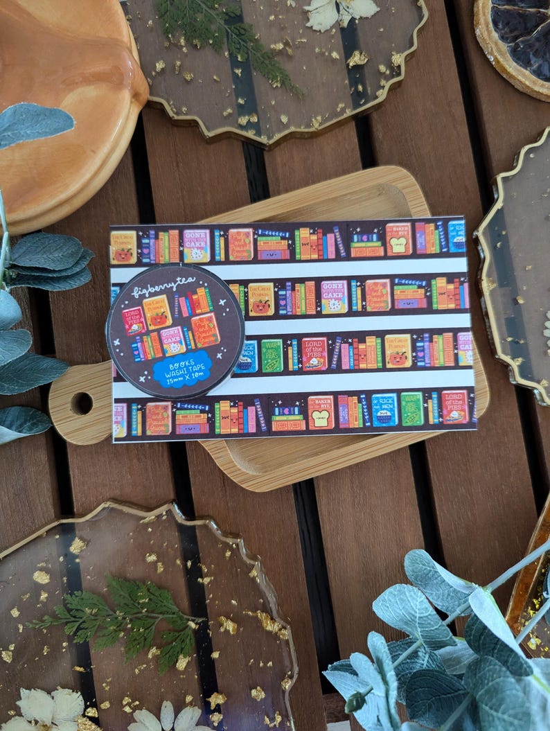 K&ouml;nnte beinhalten: Eine Rolle Washi-Tape und ein Aufkleber mit einem B&uuml;cherregal-Design mit dem Text "figberrytea". Das Klebeband ist 15 mm x 10 m gro&szlig;. Die Artikel befinden sich auf einem Holztablett und sind von dekorativen Harzuntersetzern umgeben.