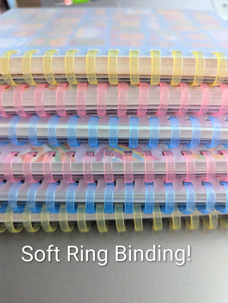 May include: Close-up of a stack of notebooks with soft ring binding. The spiral bindings are in yellow, pink, and blue. The text "Soft Ring Binding!" is at the bottom of the image.