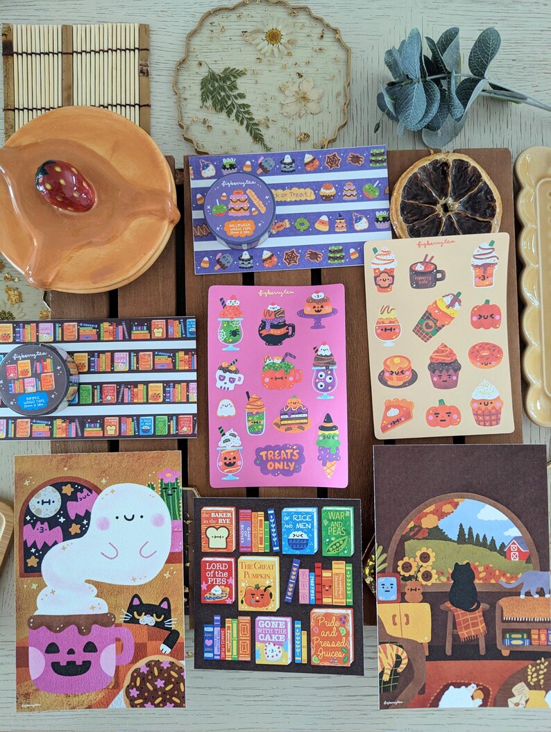 K&ouml;nnte beinhalten: Eine Sammlung von Aufklebern und Dekorationsartikeln mit Herbst- und Halloween-Motiven. Enth&auml;lt Aufkleber mit Geister-, Katzen- und K&uuml;rbisdesigns sowie einen Keramikteller und eine getrocknete Orangenscheibe. Die Aufkleber enthalten Text wie "Treats Only".