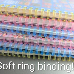 May include: A stack of notebooks with soft ring binding. The notebooks have clear plastic covers and colorful spiral bindings in yellow, pink, and blue. The text "Soft ring binding!!" is visible at the bottom of the image.