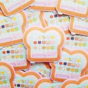 May include: A stack of colorful stickers featuring a cartoon illustration of a toaster with a variety of different food items inside. The toaster is shaped like a slice of bread and has a pink and orange color scheme. The text "Toast" and "100" are visible on the sticker.