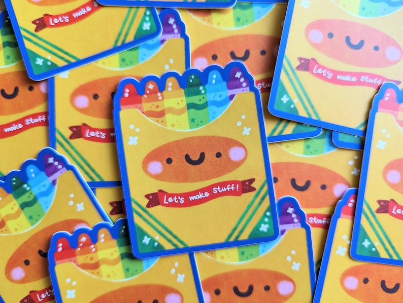 May include: A stack of yellow stickers with a blue border. Each sticker features a cartoon crayon box with a smiling face and the text "Let's make stuff!" in red and white. The crayon box is filled with colorful crayons.