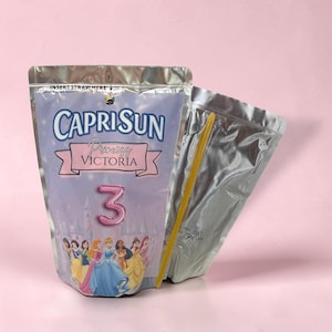 May include: A silver foil drink pouch featuring the Capri Sun logo, the text Princess Victoria, and a large pink number 3. The design includes illustrations of various princesses in front of a castle, with a yellow straw tucked behind the pouch.