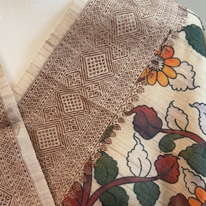 May include: A beige shawl with a brown floral pattern and a brown geometric border. The shawl is made of a soft, lightweight fabric and is perfect for adding a touch of elegance to any outfit.