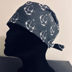Peut inclure: Un bonnet de chirurgien à motif noir et blanc. Le bonnet est sombre avec un motif blanc répété. Le bonnet est noué dans le dos. Le bonnet est présenté sur une tête de mannequin noire.