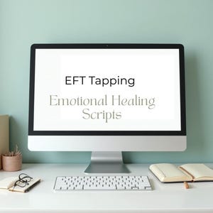May include: A desktop computer displays the text "EFT Tapping Emotional Healing Scripts" on its screen. A white keyboard, notebook, pen, and glasses are on the desk. A small potted plant and a book are also visible.