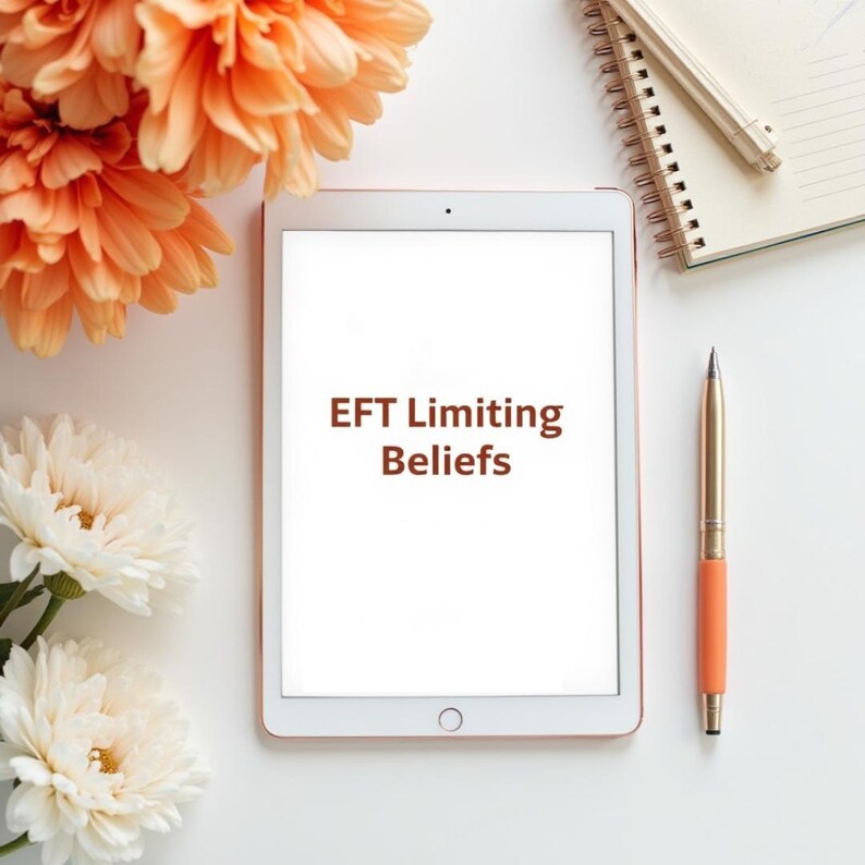 Może przedstawiać: Biały tablet z brązowym tekstem "EFT Limiting Beliefs". Złoty i pomarańczowy długopis obok, a w tle notatnik w spirali i długopis. Scena ozdobiona pomarańczowymi i białymi kwiatami.