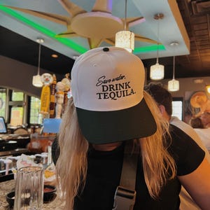 May include: White baseball cap with a green brim. The cap has black text that reads "Save water, drink tequila."