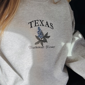 May include: Gray sweatshirt with a black embroidered design of a bluebonnet flower and the text "TEXAS Bluebonnet Flower".