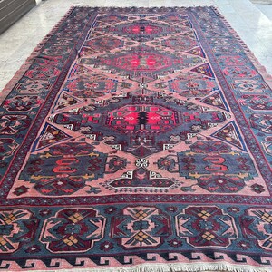 May include: A vintage Persian rug with a traditional geometric pattern in shades of pink, blue, red, and black. The rug has a fringed edge and is made of wool.