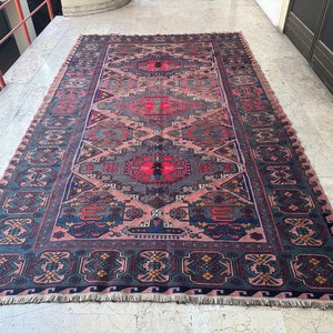 May include: A traditional Persian rug with a detailed geometric pattern in shades of blue, red, and pink. The rug has a fringed edge and is made of wool.