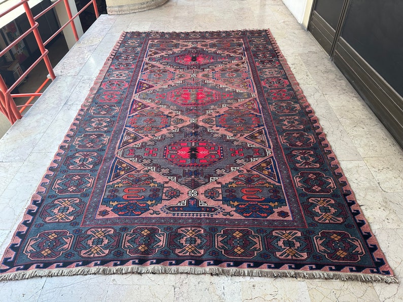 May include: A traditional Persian rug with a detailed geometric pattern in shades of blue, red, and pink. The rug has a fringed edge and is made of wool.
