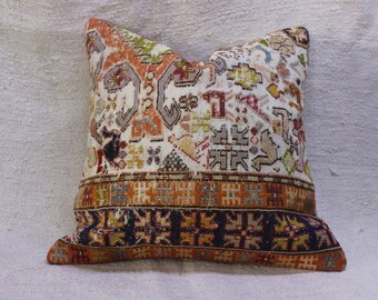 May include: A decorative pillow with a white background and a colorful geometric pattern. The pillow has a brown, orange, and blue border.