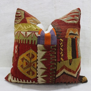 May include: A square decorative pillow with a patchwork design. The pillow features a variety of colors including red, yellow, orange, and purple. The pillow has a textured appearance and is likely made of fabric.