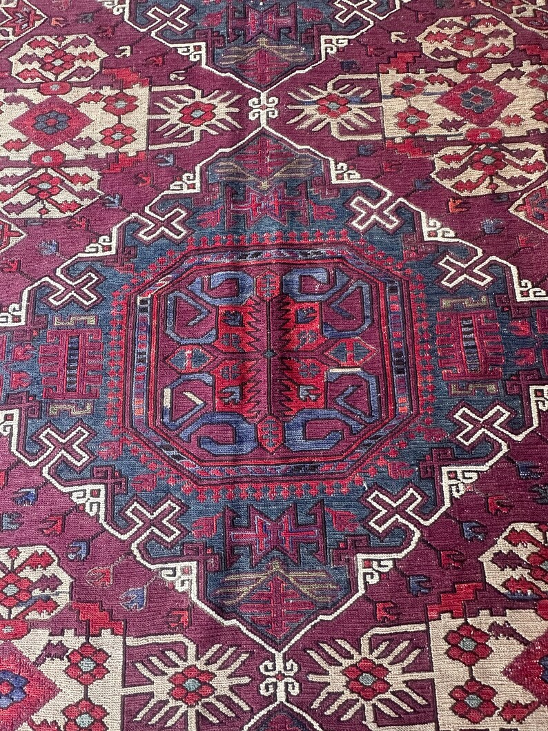 May include: A vintage rug with a traditional Persian design. The rug features a central medallion with intricate geometric patterns in shades of red, blue, and cream. The rug is woven with a high-quality wool and has a soft, luxurious feel.
