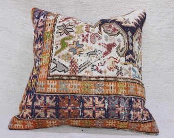May include: A decorative pillow with a colorful geometric pattern in shades of orange, blue, green, and white. The pillow has a traditional design with intricate details.