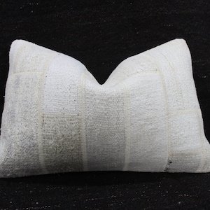 May include: Rectangular white pillow with a textured surface. The pillow has a patchwork design with vertical and horizontal lines. The pillow is made of a soft, woven material and is set against a black background.