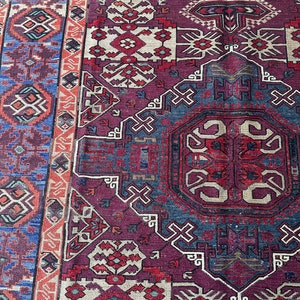 May include: A vintage rug with a detailed geometric pattern in shades of red, blue, and white. The rug has a central medallion and a border with intricate designs.