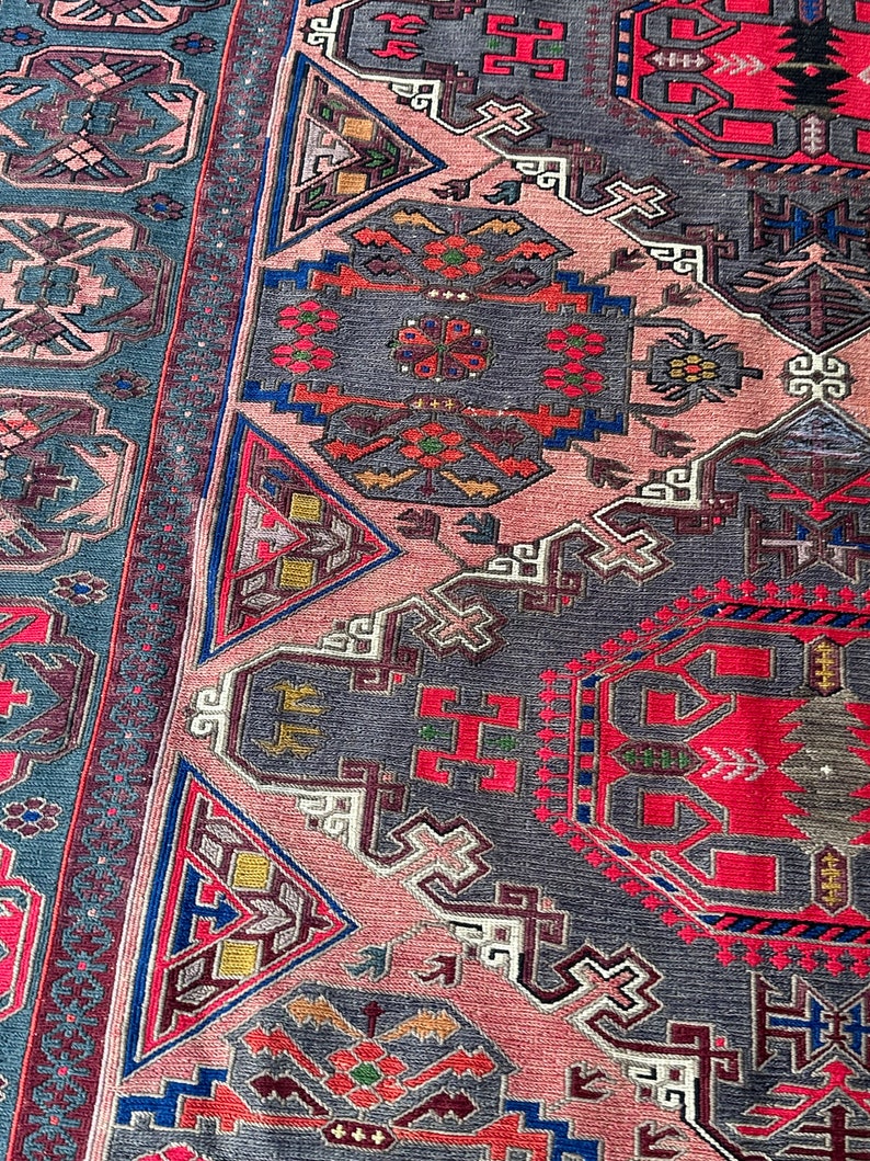 May include: A close-up of a traditional rug with intricate geometric patterns in shades of red, blue, pink, and gray. The rug features a repeating design of triangles, squares, and other shapes.