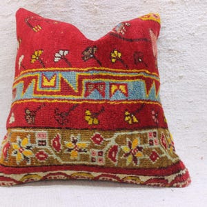 May include: Red, blue and yellow patterned throw pillow with a geometric design. The pillow is made of woven fabric and has a fringed edge.
