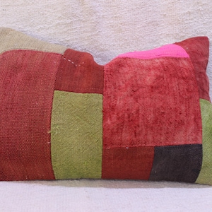 Puede incluir: Una almohada rectangular de patchwork con cuadrados de tela roja, verde y rosa. La almohada está hecha de un material suave y texturizado.
