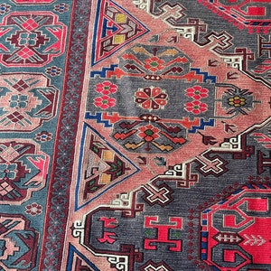 May include: A close-up of a traditional rug with intricate geometric patterns in shades of red, blue, pink, and gray. The rug features a repeating design of triangles, squares, and crosses.