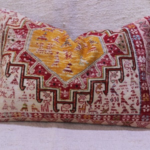 May include: A decorative pillow with a colorful geometric pattern in shades of red, yellow, white, and blue. The pillow is made of a woven fabric with a traditional design.