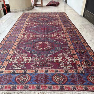 May include: A traditional Persian rug with a colorful geometric pattern in shades of red, blue, and cream. The rug has a fringe border and is made of wool.