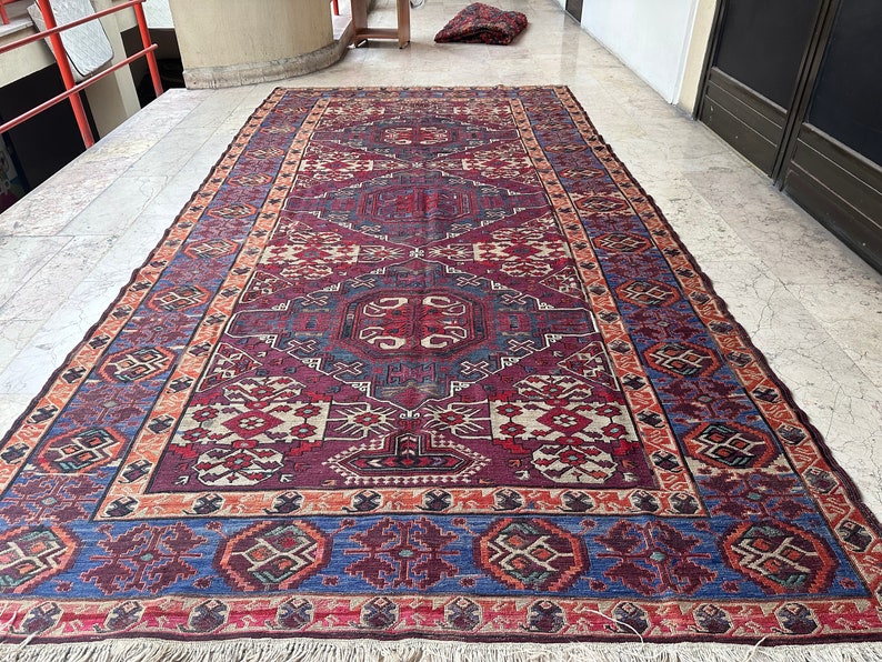 May include: A traditional Persian rug with a colorful geometric pattern in shades of red, blue, and cream. The rug has a fringe border and is made of wool.