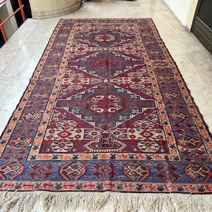 May include: A traditional Persian rug with a rich, intricate design featuring a central medallion and repeating geometric patterns in shades of red, blue, and beige. The rug has a fringe border.