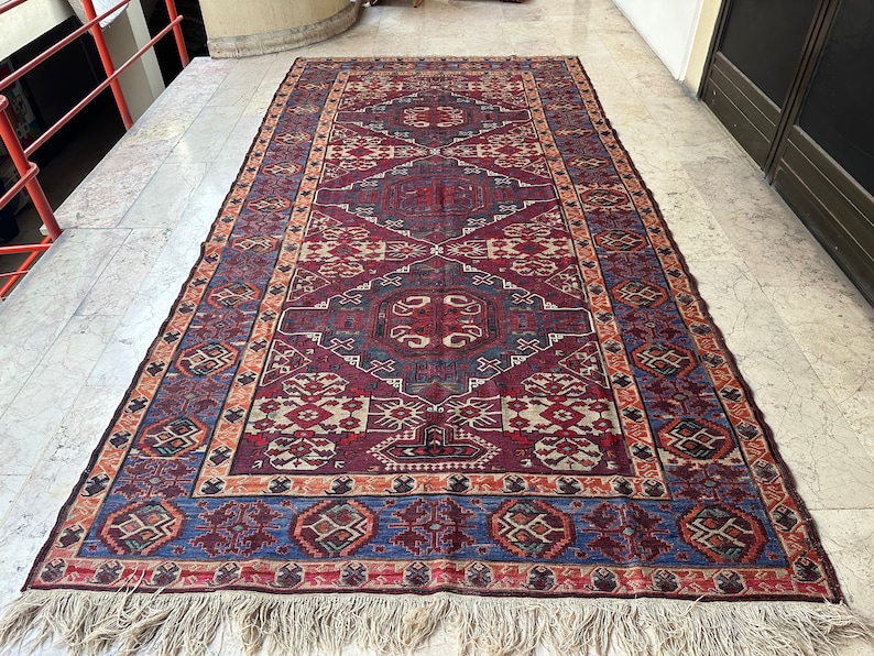 May include: A traditional Persian rug with a rich, intricate design featuring a central medallion and repeating geometric patterns in shades of red, blue, and beige. The rug has a fringe border.