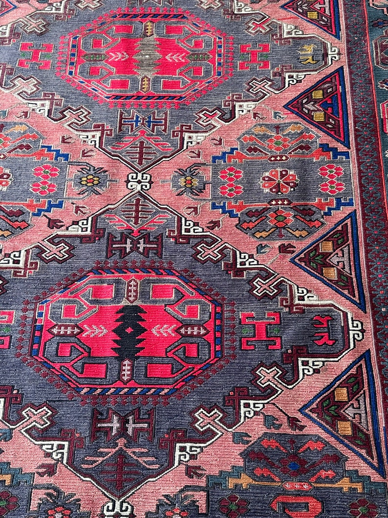 May include: A traditional rug with a geometric pattern in shades of pink, red, blue, and gray. The rug features intricate details and a central medallion.