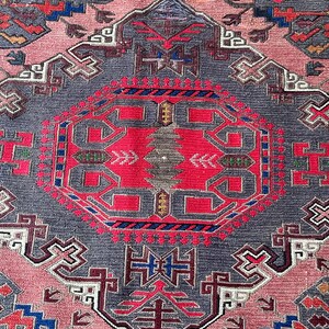 May include: A close-up of a pink and gray rug with intricate geometric patterns in shades of red, blue, and green. The rug has a traditional design with a central medallion and repeating motifs.