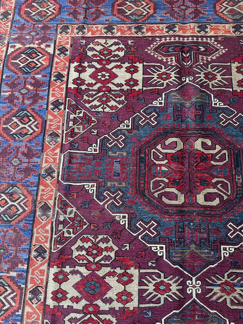 May include: A vintage rug with a detailed geometric pattern in shades of red, blue, and white. The rug has a central medallion and a border with intricate designs.