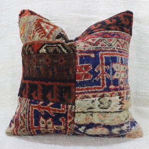 Op de afbeelding: Een patchwork kussenhoes met verschillende kleurrijke patronen in tinten rood, blauw, bruin en wit. De kussenhoes is gemaakt van een geweven stof met een textuur.