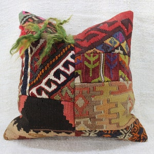 May include: A colorful patchwork pillow with a variety of geometric patterns in shades of red, green, brown, and beige. The pillow has a frayed edge and a textured surface.