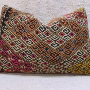 May include: A colourful pillow cover with a geometric pattern in shades of brown, orange, pink, yellow, and black. The pattern is made up of squares and diamonds.