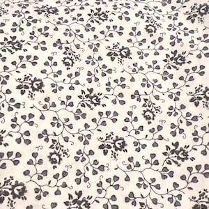 May include: Cream-colored fabric with a repeating pattern of dark gray floral and vine motifs. The design features stylized flowers and heart-shaped leaves, creating a delicate and vintage aesthetic. The fabric is densely patterned.