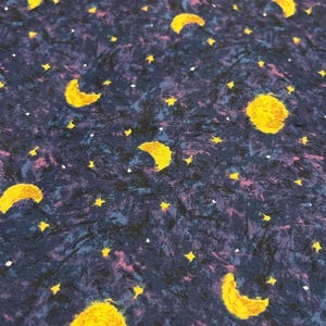 May include: Fabric with a night sky design. The fabric features yellow moons and stars against a dark blue background with hints of purple and white. The design has a painted or textured appearance.