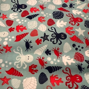 May include: A light blue fabric with a repeating pattern of marine life. The design includes red starfish, octopuses, and coral, along with white seashells and dark blue crabs and shells. The overall theme is nautical.