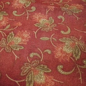 Peut inclure: Gros plan sur un tissu rouge avec un motif floral. Le motif présente de grandes fleurs dans des tons de marron, pêche et rouge, avec des vignes délicates et courbes. Le tissu a un aspect texturé, suggérant un matériau tissé.