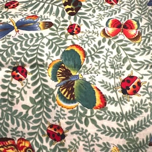 May include: A fabric pattern featuring colorful butterflies and ladybugs scattered across a cream-colored background with green leaf designs. The butterflies have intricate wing patterns in shades of orange, yellow, green, and blue.