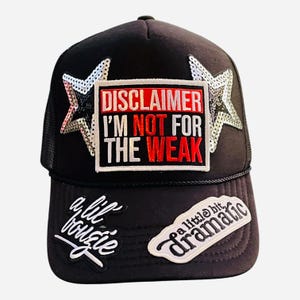May include: Black trucker hat with a silver sequin star on each side. The hat has a red, white, and black patch that says "DISCLAIMER I'M NOT FOR THE WEAK". There are two other patches on the front of the hat, one that says "a lil bougie" and another that says "a little bit dramatic".