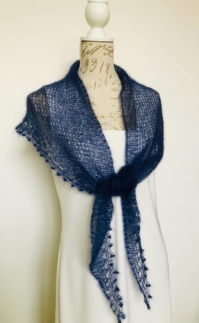 May include: A dark navy blue triangular shawl crafted from a fine, sheer, open-knit yarn. The accessory features a delicate, airy texture with small decorative loops along the edges and is tied in a simple knot at the center front of the display.