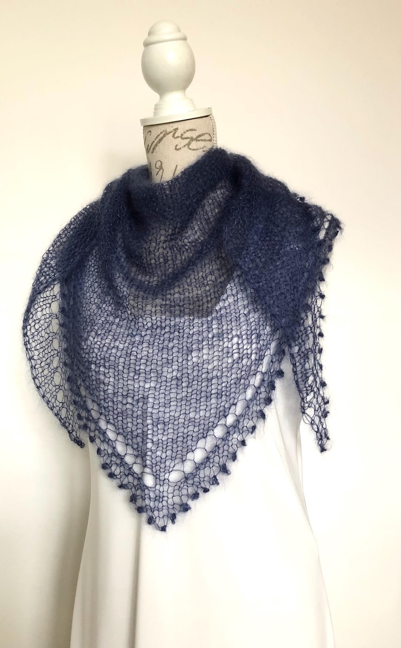 May include: A dark blue triangular shawl crafted with a loose, open-knit texture. The garment features a delicate, airy construction with a decorative scalloped edge along the bottom border, showcasing a fine, fuzzy yarn finish throughout.