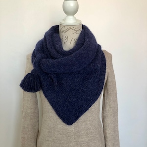 Puede incluir: Una bufanda de punto azul oscuro con un borla en un extremo. La bufanda está drapeada sobre un maniquí blanco con un suéter beige.